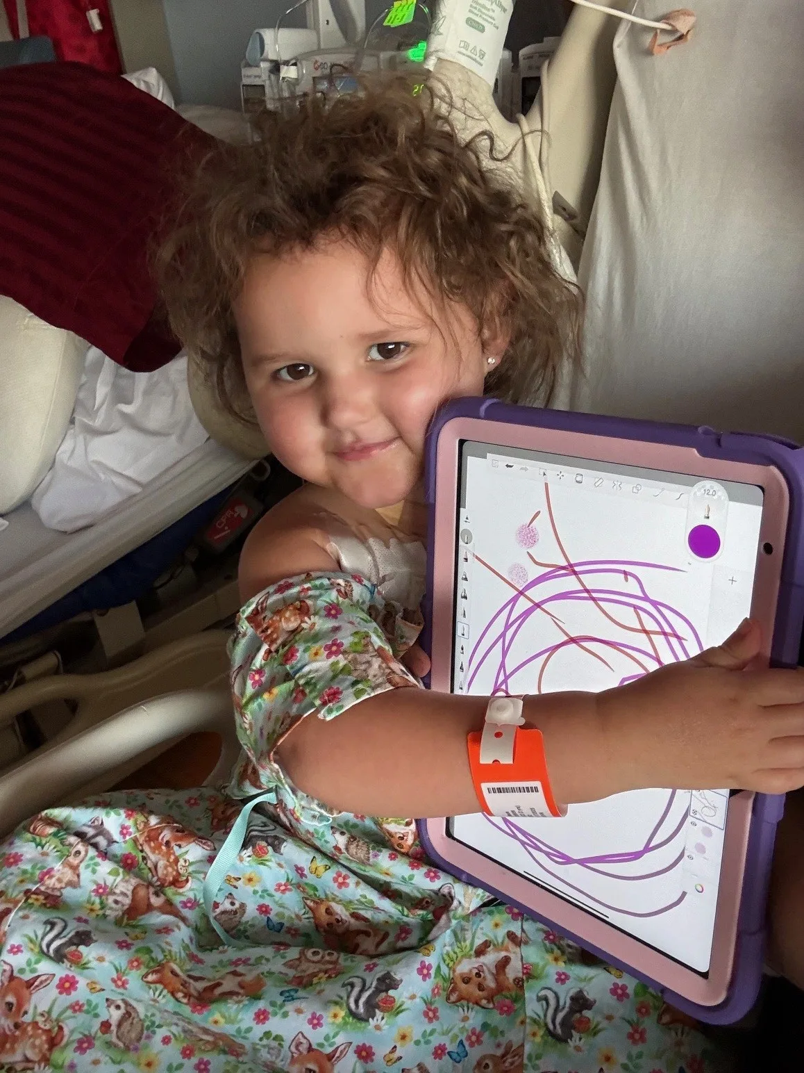 A smiling child in a hospital room hugging a teddy bear